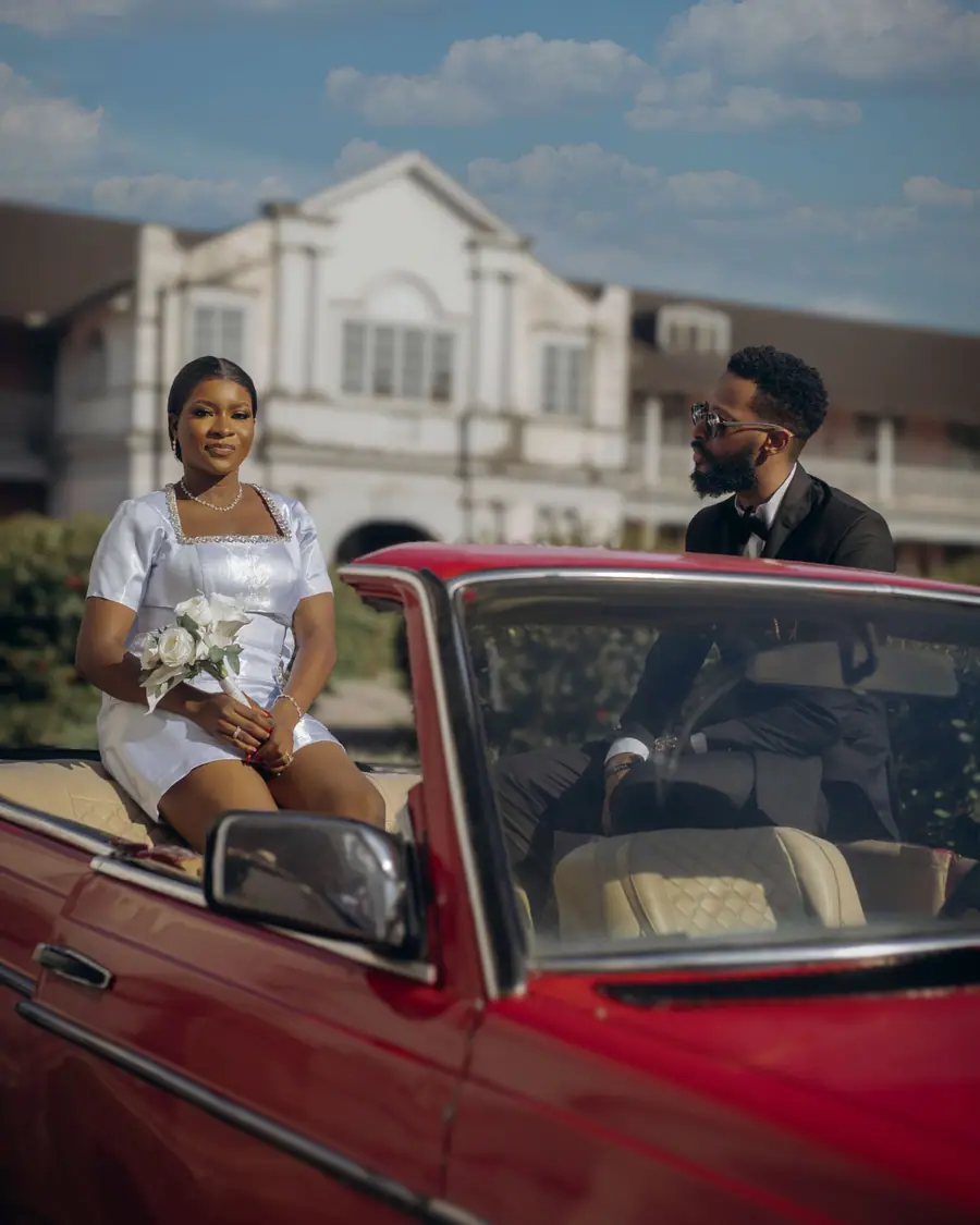 Amara in her white dress seated on the red convertible with a bouquet
